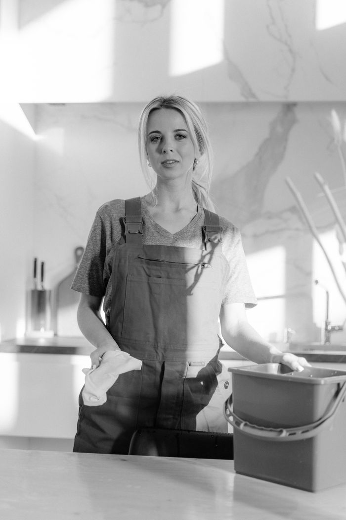 Monochrome image of a housekeeper holding cleaning tools within a contemporary kitchen space.